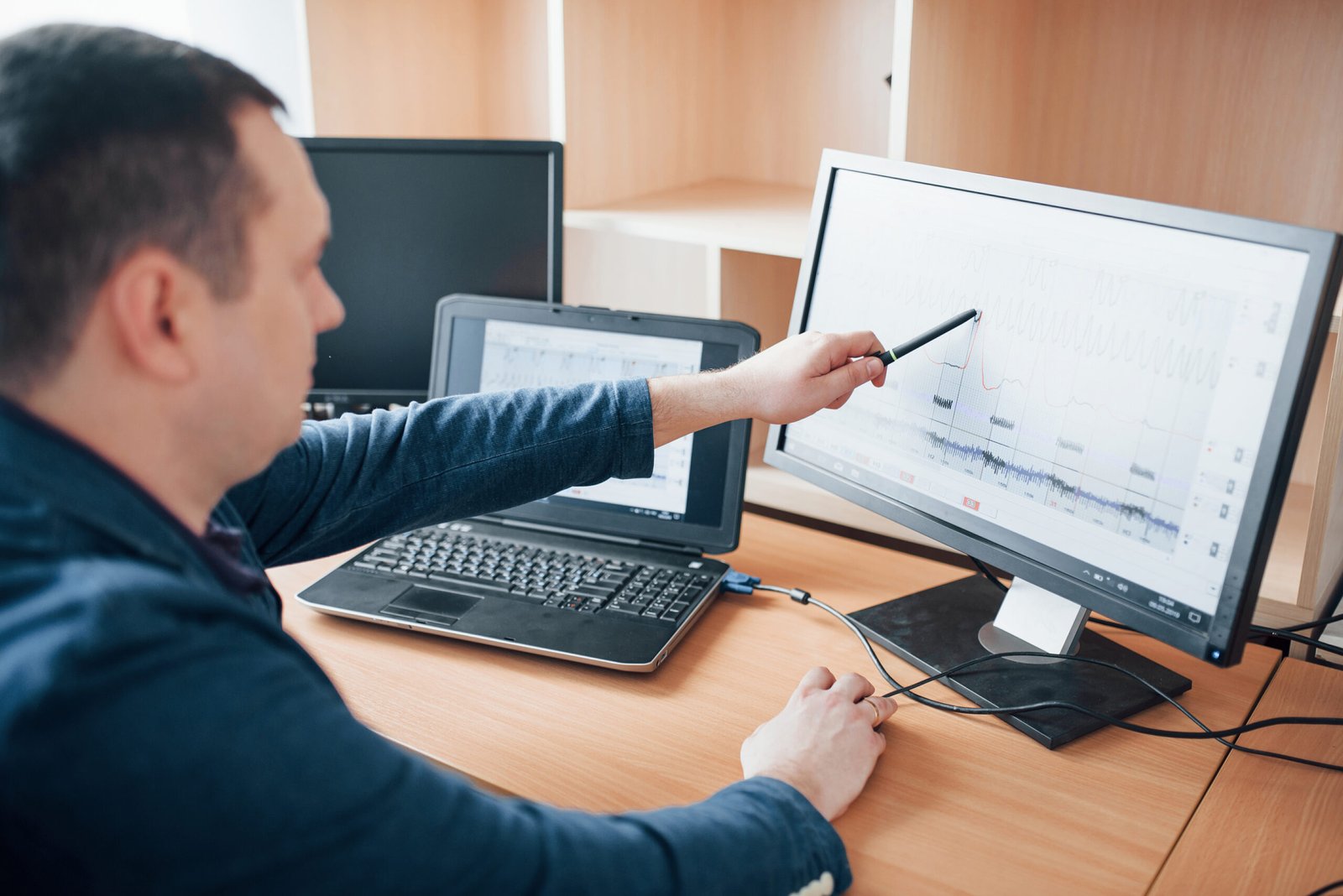 Showing peak of curve in diagram. Polygraph examiner works in the office with his lie detector's equipment.